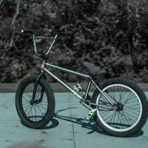 Silver BMX bike on a skatepark surface, trees in background.