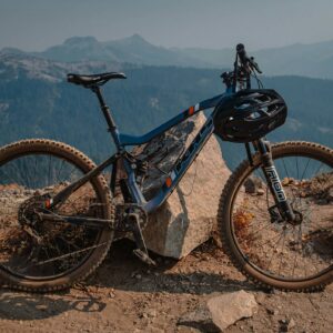 Mountain bike with helmet on handlebars, leaning against a rock on a dirt trail, with misty mountains in the background.